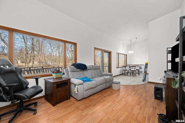 living area featuring baseboards, high vaulted ceiling, light wood finished floors, and a notable chandelier