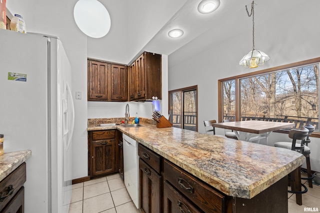 kitchen with hanging light fixtures, light tile patterned flooring, a sink, white appliances, and a peninsula