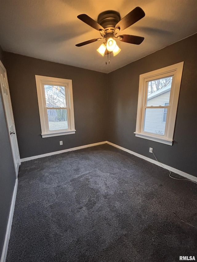 spare room featuring a healthy amount of sunlight, baseboards, dark colored carpet, and a ceiling fan