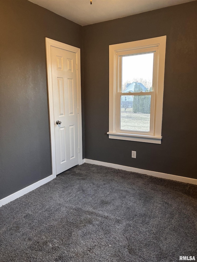 unfurnished room featuring dark carpet and baseboards