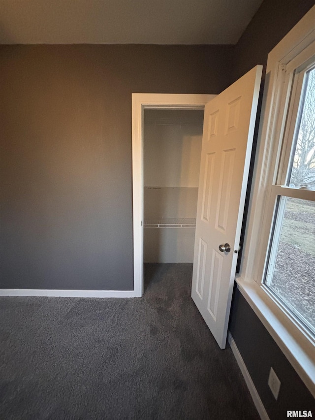 unfurnished bedroom with dark carpet and baseboards