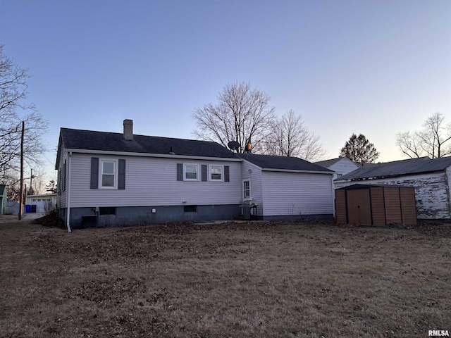 back of house featuring an outdoor structure, a chimney, and a storage unit