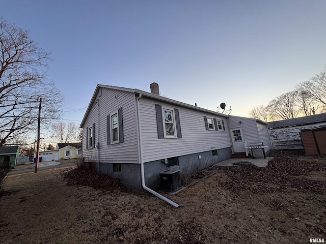 back of house at dusk featuring entry steps, a chimney, and central AC