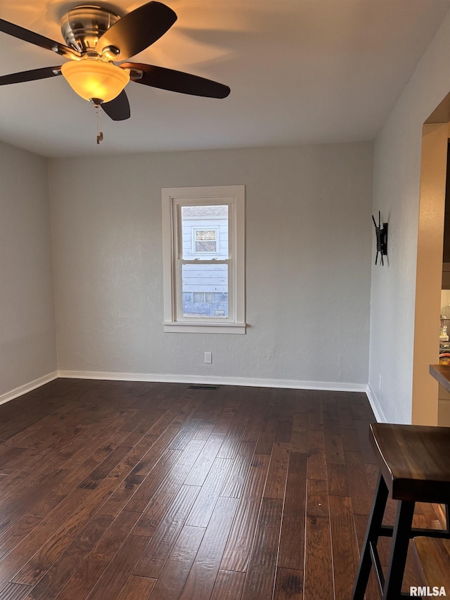 spare room featuring dark wood finished floors, a ceiling fan, and baseboards