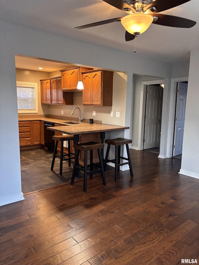 kitchen with dark wood finished floors, a breakfast bar, a peninsula, light countertops, and a sink