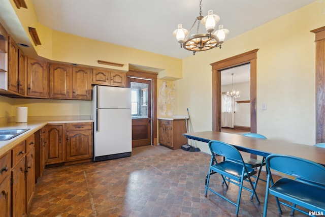 kitchen featuring decorative light fixtures, brown cabinets, freestanding refrigerator, and a chandelier