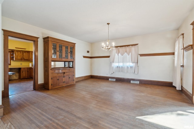 empty room with hardwood / wood-style floors, an inviting chandelier, baseboards, and visible vents