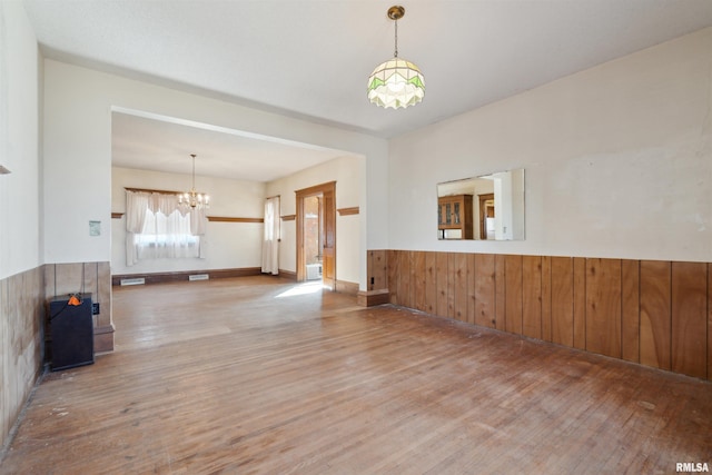 empty room with a wainscoted wall, wood walls, an inviting chandelier, and wood finished floors