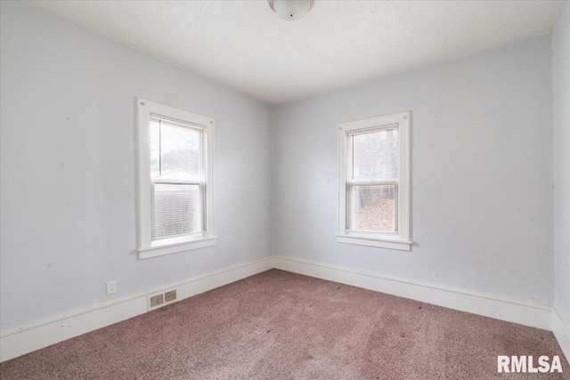 empty room featuring carpet floors, visible vents, a textured ceiling, and baseboards