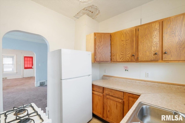 kitchen featuring arched walkways, light carpet, white appliances, visible vents, and light countertops