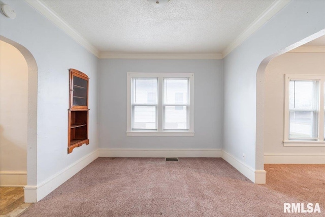 carpeted empty room featuring arched walkways, crown molding, and a textured ceiling