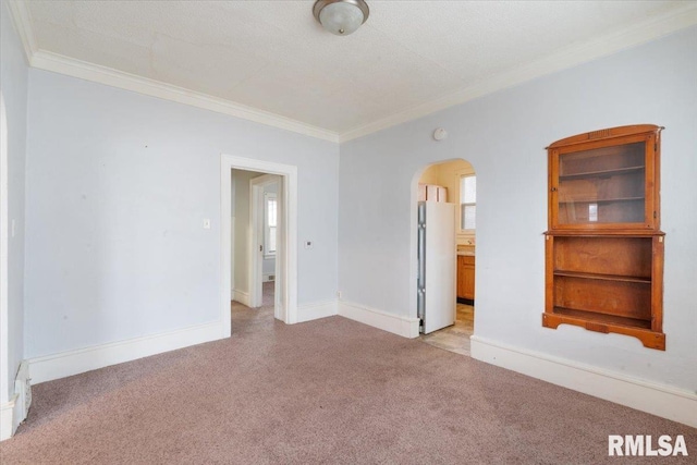 spare room featuring arched walkways, light colored carpet, baseboards, a wealth of natural light, and crown molding