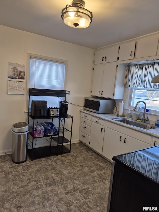 kitchen with white cabinetry, stainless steel microwave, light countertops, and a sink