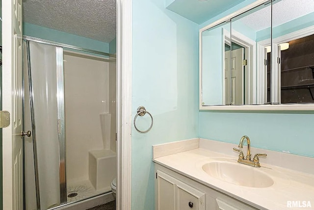 full bath with a textured ceiling, a stall shower, vanity, and toilet