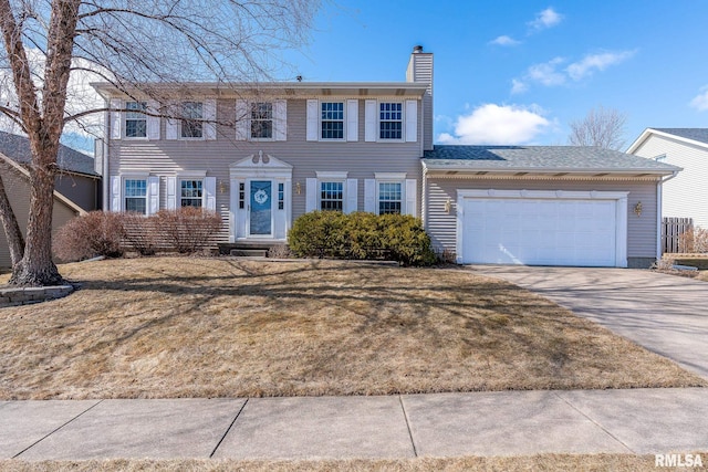 colonial house with an attached garage, driveway, a chimney, and a front lawn