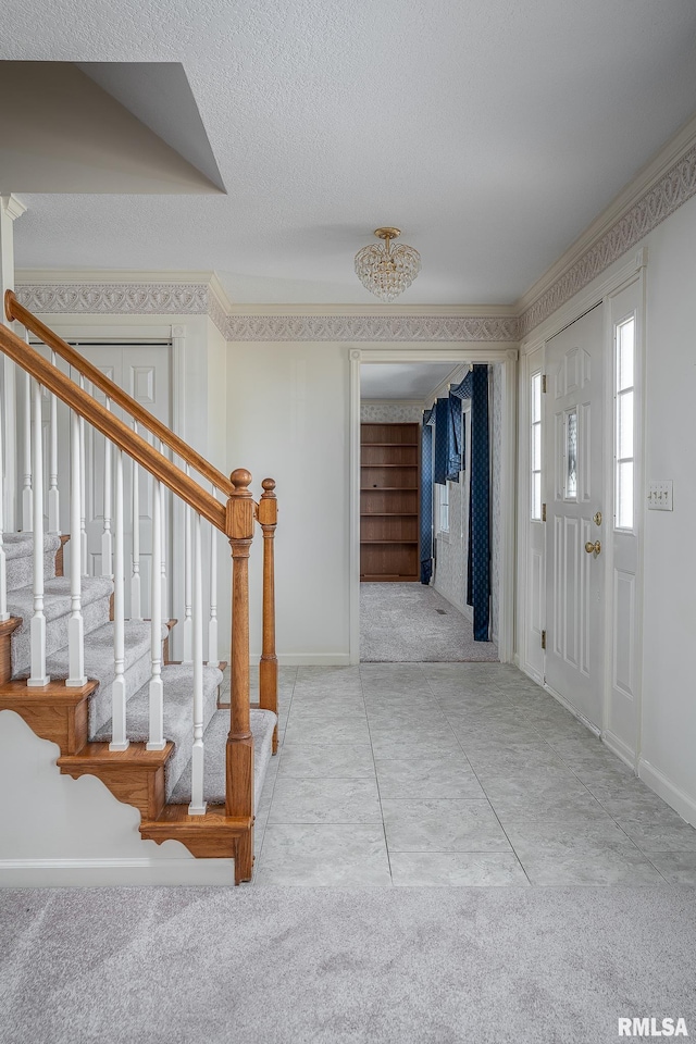 entrance foyer featuring carpet, stairway, ornamental molding, a textured ceiling, and baseboards