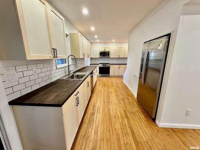 kitchen featuring tasteful backsplash, baseboards, appliances with stainless steel finishes, light wood-type flooring, and a sink