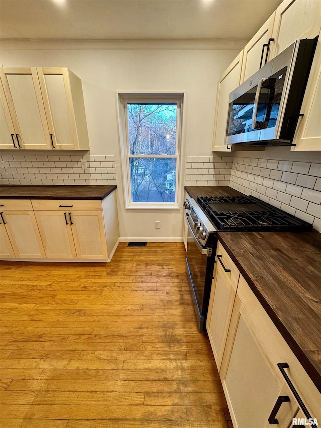 kitchen featuring baseboards, wood counters, appliances with stainless steel finishes, light wood-style floors, and backsplash