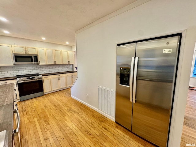 kitchen with visible vents, light wood-style floors, appliances with stainless steel finishes, decorative backsplash, and dark countertops