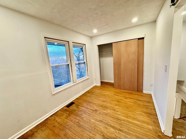 unfurnished bedroom with a textured ceiling, visible vents, baseboards, a closet, and light wood-type flooring