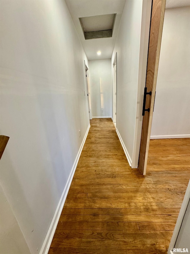 hallway with wood finished floors, attic access, and baseboards