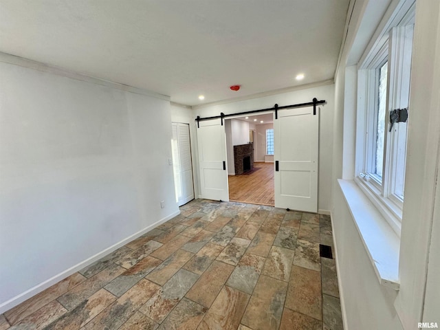 unfurnished room featuring a barn door, baseboards, stone tile flooring, and recessed lighting