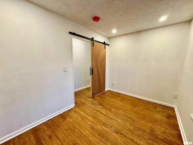 spare room with recessed lighting, a barn door, a textured ceiling, baseboards, and hardwood / wood-style flooring