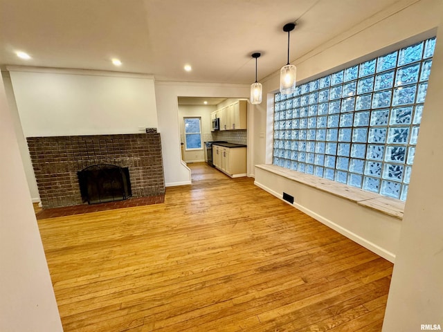 unfurnished living room with light wood-type flooring, a brick fireplace, crown molding, and baseboards