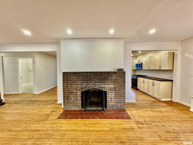 living room featuring recessed lighting, a fireplace, baseboards, ornamental molding, and light wood-type flooring