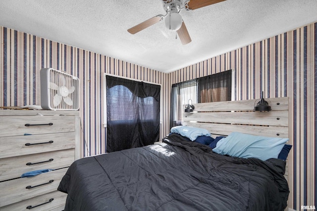 bedroom featuring a textured ceiling, ceiling fan, and wallpapered walls