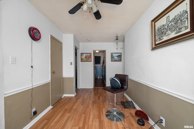 hall with light wood-style flooring, baseboards, and a textured ceiling