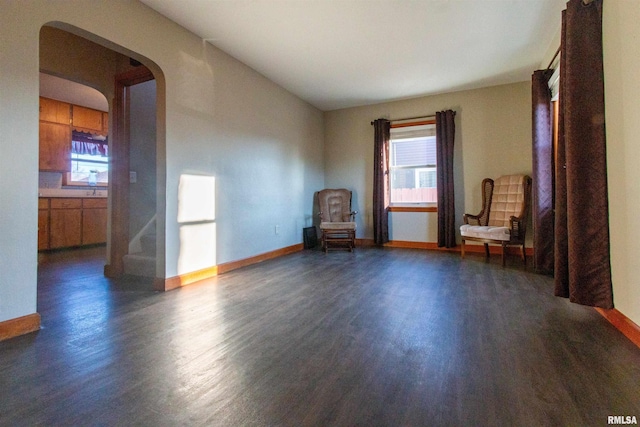 unfurnished room featuring baseboards, plenty of natural light, arched walkways, and wood finished floors