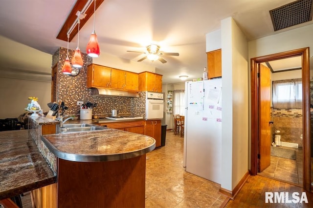 kitchen featuring a peninsula, white appliances, a sink, visible vents, and brown cabinets