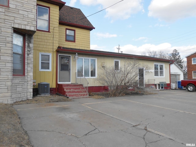 view of front facade with entry steps, stone siding, roof with shingles, and central air condition unit