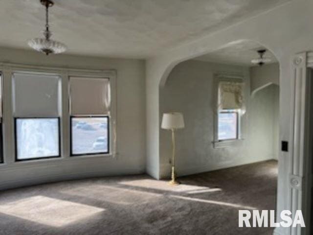 carpeted empty room featuring arched walkways