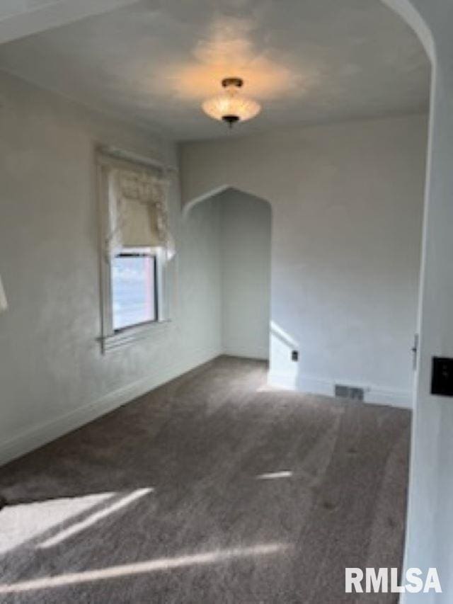 empty room with carpet floors, baseboards, visible vents, and arched walkways