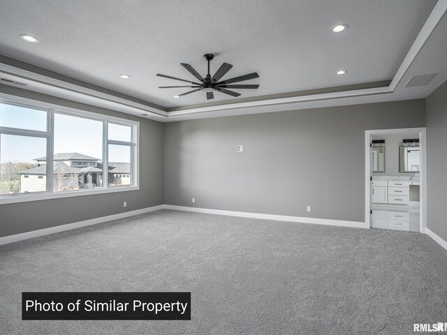 unfurnished bedroom with a textured ceiling, carpet floors, a tray ceiling, and baseboards