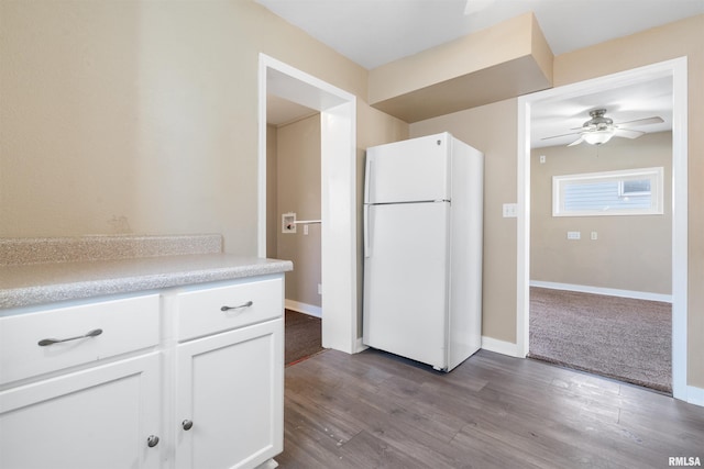 kitchen featuring light countertops, dark wood-type flooring, freestanding refrigerator, white cabinetry, and baseboards