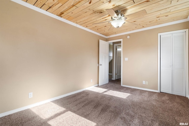 unfurnished bedroom with baseboards, wood ceiling, carpet, crown molding, and a closet