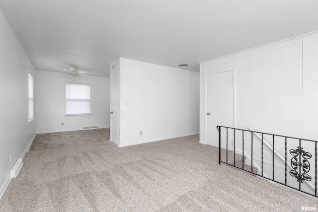 carpeted spare room with a ceiling fan, visible vents, a textured ceiling, and baseboards