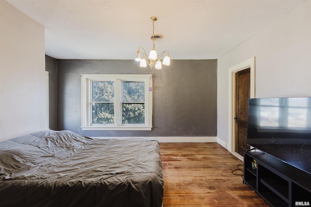 bedroom with visible vents, a notable chandelier, baseboards, and wood finished floors