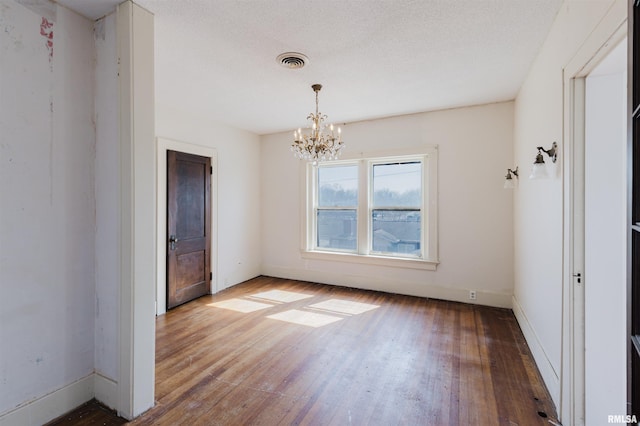 empty room with visible vents, baseboards, wood-type flooring, a textured ceiling, and a notable chandelier