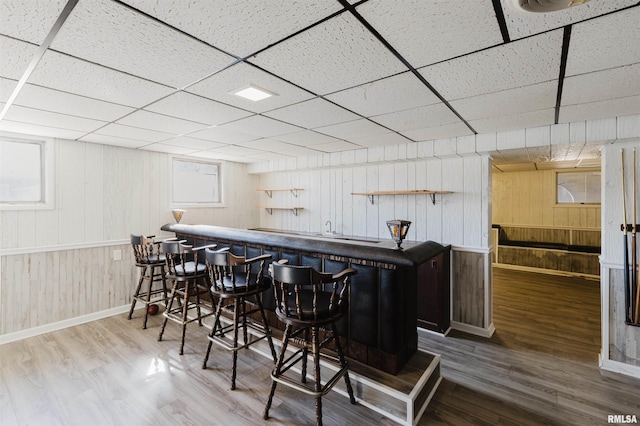 bar with a bar, wood walls, wood finished floors, and a paneled ceiling