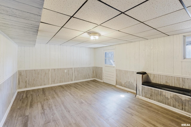 below grade area with a paneled ceiling, plenty of natural light, wood walls, and wood finished floors