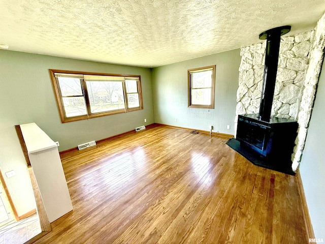 unfurnished living room featuring baseboards, visible vents, wood finished floors, a wood stove, and a textured ceiling