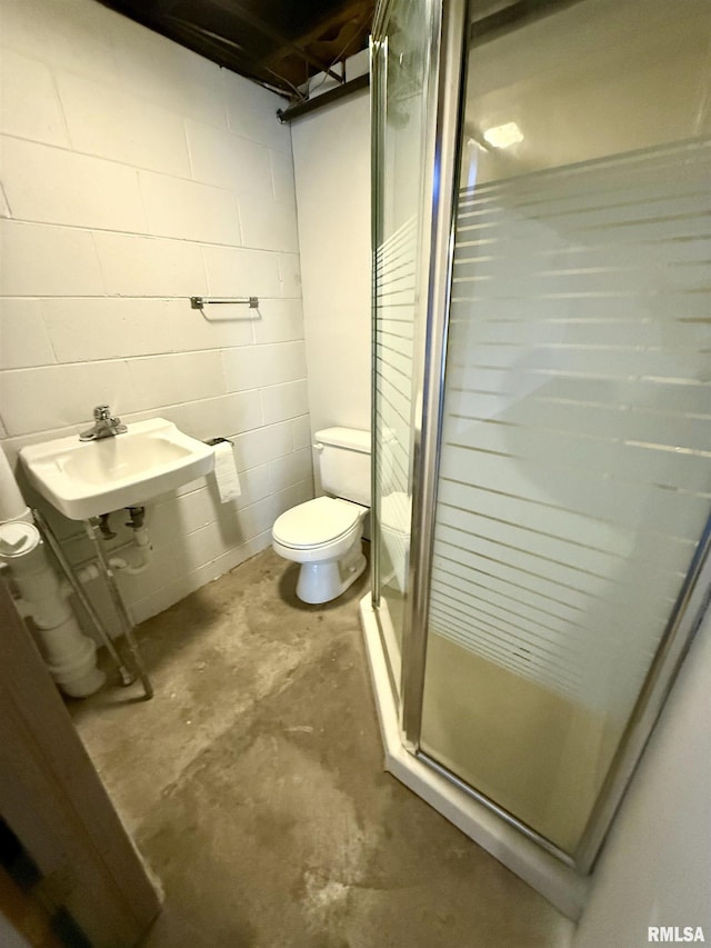 bathroom featuring concrete block wall, unfinished concrete flooring, toilet, a shower stall, and a sink