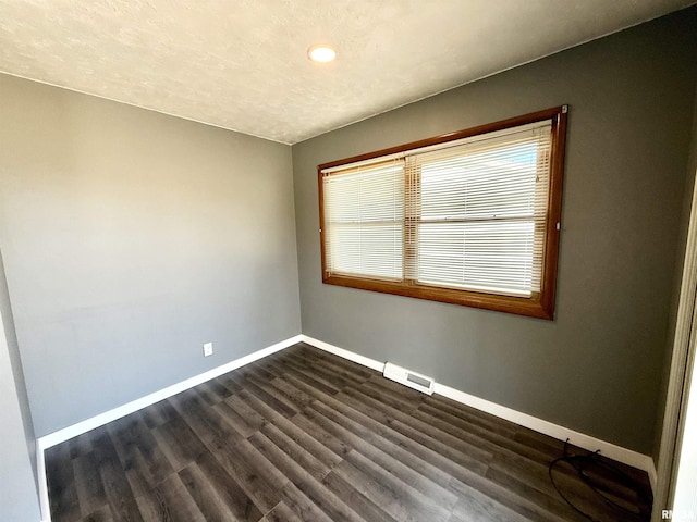 empty room with a textured ceiling, dark wood-type flooring, visible vents, and baseboards