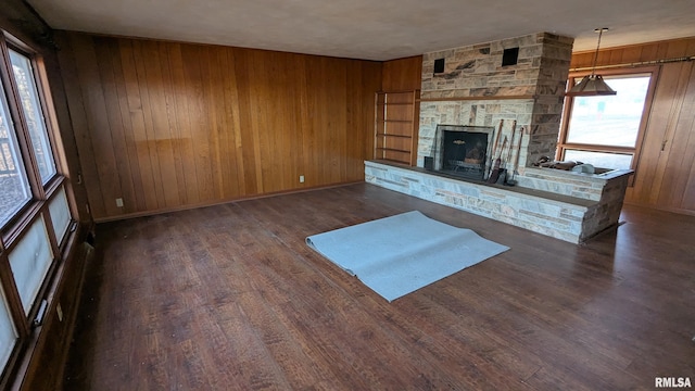 interior space with wooden walls, a stone fireplace, baseboards, and wood finished floors