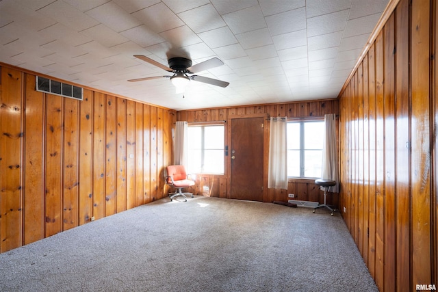 empty room with wood walls, carpet, visible vents, and ceiling fan