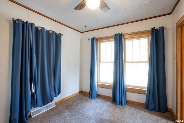 empty room featuring ceiling fan, carpet floors, visible vents, and crown molding